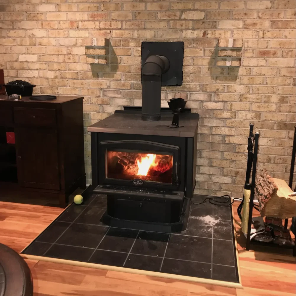 Installed freestanding wood stove in Norfolk, VA featuring double-wall pipe, non-combustible pad, and approved wall shielding.